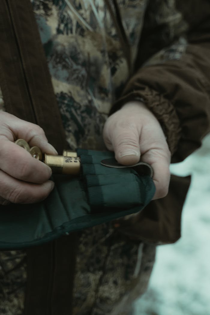 Close-up of a hunter loading shotgun shells into a leather pouch outdoors.